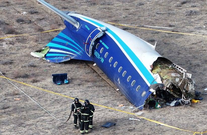 Pedaço da traseira de um avião no chão, com dois bombeiros no local, em meio à investigação sobre o possível envolvimento do sistema anti-aéreo russo.