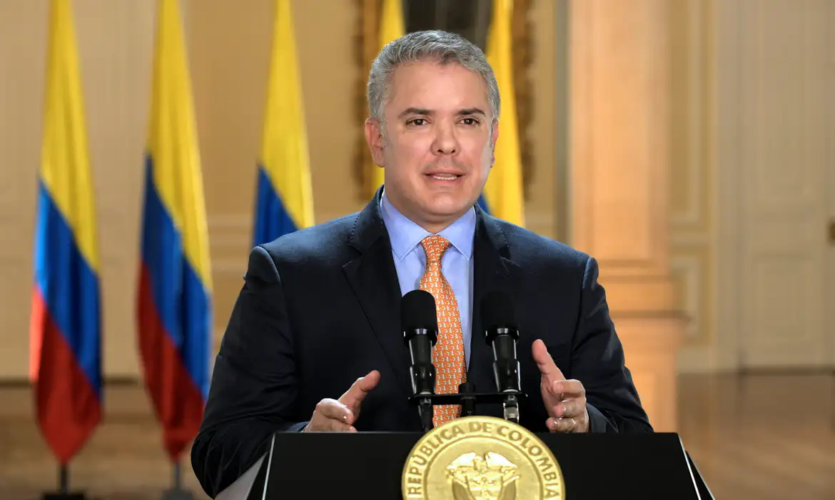 Ex-presidente colombiano Iván Duque durante discurso sobre intervenção humanitária na Venezuela, com a bandeira da Colômbia ao fundo.