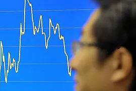 Homem passa em frente a um gráfico que mostra a oscilação do Índice Hang Seng em Hong Kong.