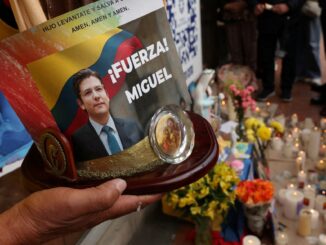 Homem segura imagem da Virgem Maria e foto do senador colombiano Miguel Uribe Turbay em frente ao hospital Santa Fe, em Bogotá.