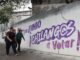 Mulheres passam por propaganda eleitoral pintada em muro em Cidade do México, maio de 2025