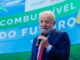 Presidente Lula discursa com microfone em evento sobre políticas energéticas, diante de painel com os dizeres "Combustível do Futuro".