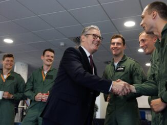 Primeiro-ministro Keir Starmer apertando a mão de militar da RAF Valley, com outros militares uniformizados ao redor sorrindo.