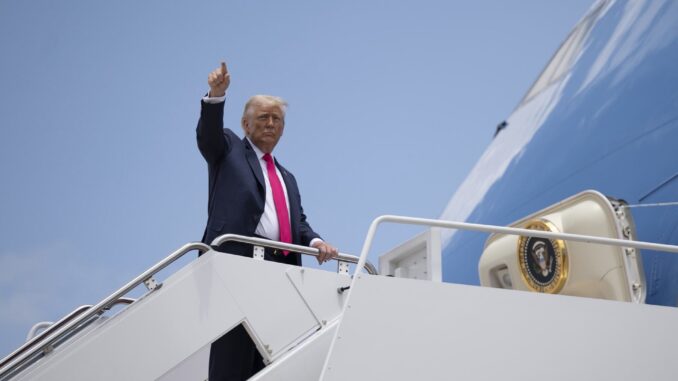 Donald Trump acenando com o polegar para cima ao embarcar em avião presidencial sob céu azul claro.