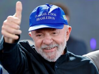 Homem sorridente com barba branca usando boné azul escrito “O Brasil é dos brasileiros” e fazendo sinal de positivo com o polegar.
