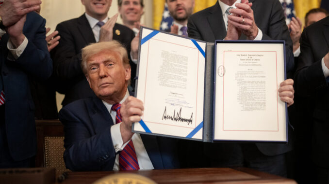 Presidente dos EUA exibindo documento assinado durante cerimônia na Casa Branca, cercado por autoridades e membros do governo aplaudindo.