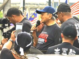 Ex-primeiro-ministro malaio Dr. Mahathir Mohamad discursando em protesto #TurunAnwar na Praça Merdeka, Kuala Lumpur, cercado por apoiadores com bandeiras da Malásia.