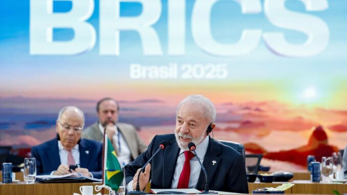 Presidente Lula discursando em reunião do BRICS no Brasil em 2025, com a bandeira brasileira à frente e painel com o logo do BRICS ao fundo.