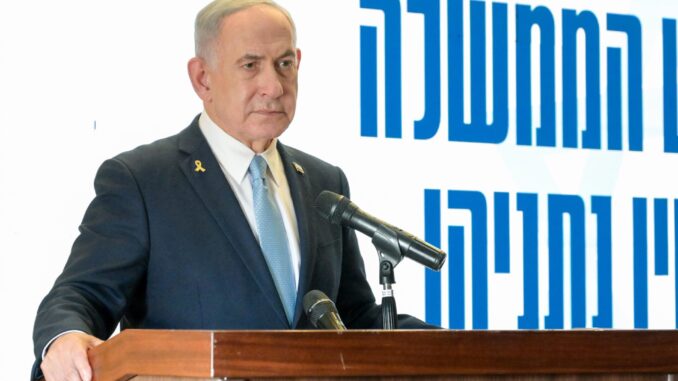 Benjamin Netanyahu em discurso oficial, vestindo terno escuro e gravata azul clara, falando em um púlpito com microfones, com fundo branco e texto em hebraico azul.