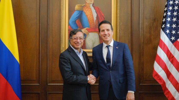 Presidente colombiano Gustavo Petro cumprimenta representante dos EUA em encontro oficial em Bogotá, com bandeiras da Colômbia e dos EUA ao fundo.