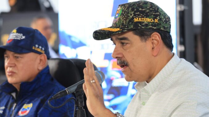 Nicolás Maduro usando boné militar enquanto fala ao microfone, acompanhado de outro oficial, em evento de mobilização de milícias na Venezuela.