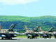 Três caças F-16 da Força Aérea Israelense alinhados em pista de aeroporto com pilotos e técnicos próximos, com colinas verdes ao fundo.