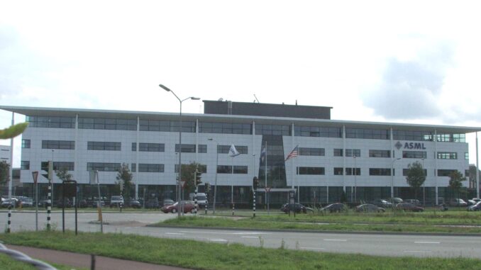 Prédio moderno da sede da ASML em Veldhoven, Holanda, com fachada branca e janelas de vidro, mostrando bandeiras na frente e carros estacionados ao redor.