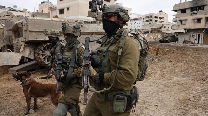 Tropas das Forças de Defesa de Israel (IDF) armadas avançam na Cidade de Gaza com um cão de detecção, próximo a prédios destruídos e veículos militares.