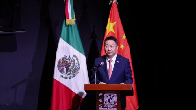 Representante da China discursando em frente às bandeiras do México e da China em evento oficial.