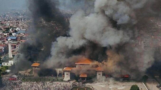 Edifício do Parlamento do Nepal em chamas durante protestos em Kathmandu; grande fumaça negra sobe ao céu enquanto manifestantes se reúnem na frente do prédio.