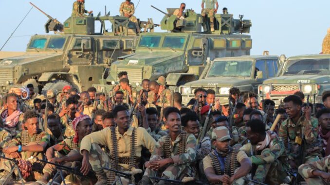 Soldados das Forças Armadas Nacionais Somalis posando em grupo na frente de veículos militares, durante cerimônia de homenagem após vitória contra o Al-Shabaab.