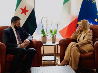 Encontro entre Ahmed al-Sharaa, presidente da Síria, e representante italiana durante a Semana de Alto Nível da Assembleia Geral da ONU, com bandeiras da Síria, Itália e União Europeia ao fundo.
