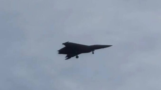 Foto do caça chinês de sexta geração J-50 em voo de teste, com trem de pouso parcialmente recolhido, sob céu nublado.