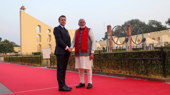 “Primeiro-ministro indiano Narendra Modi e presidente francês Emmanuel Macron apertando mãos em frente a instrumentos astronômicos históricos em Jaipur, Índia.