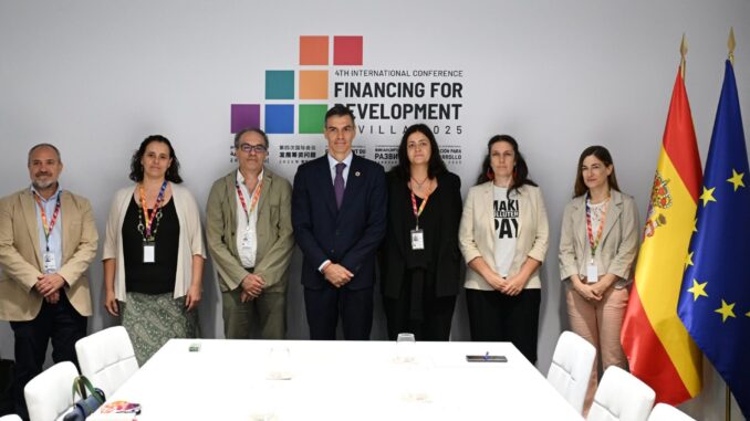 Pedro Sánchez posa com delegados em conferência internacional de financiamento para desenvolvimento, com bandeiras da Espanha e da União Europeia ao fundo.
