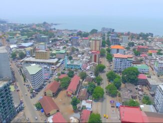 Vista aérea de Conacri, Guiné, mostrando prédios, ruas movimentadas e a orla costeira em um dia claro.