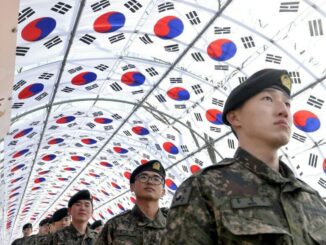 Soldados sul-coreanos em uniformes militares marcham sob um túnel decorado com bandeiras da Coreia do Sul (Taegeukgi) durante uma visita ao Salão da Independência.