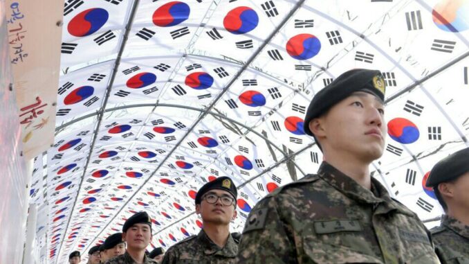 Soldados sul-coreanos em uniformes militares marcham sob um túnel decorado com bandeiras da Coreia do Sul (Taegeukgi) durante uma visita ao Salão da Independência.