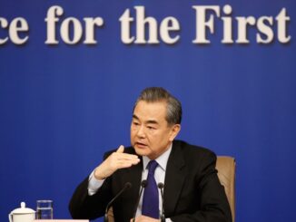 Wang Yi, ministro das Relações Exteriores da China, falando em uma conferência, usando terno escuro e gravata, gesticulando com a mão direita.