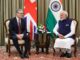 Keir Starmer e Narendra Modi sentados lado a lado durante reunião oficial, com as bandeiras do Reino Unido e Índia ao fundo, discutindo relações comerciais e econômicas.
