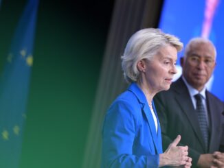 Ursula von der Leyen em pronunciamento, com bandeira da União Europeia ao fundo