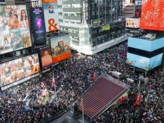 Manifestantes protestam em Nova York contra o governo de Donald Trump, segurando cartazes e bandeiras.
