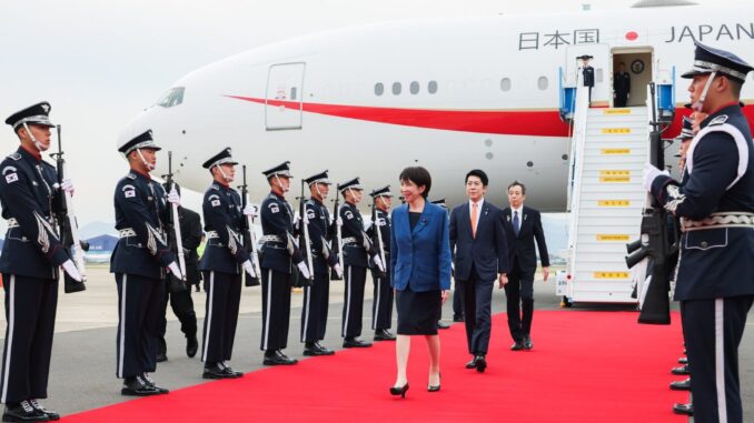 Primeira-ministra japonesa Sanae Takaichi caminhando pelo tapete vermelho, recebida por soldados durante sua chegada à Coreia do Sul para a cúpula da APEC 2025.