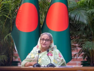 Sheikh Hasina em um evento oficial, usando um lenço tradicional, com expressão séria, simbolizando o fim de seus 15 anos no poder em Bangladesh.