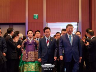 Presidente chinês Xi Jinping e presidente sul-coreano caminhando juntos em evento da APEC 2025, cercados por delegados e assessores.