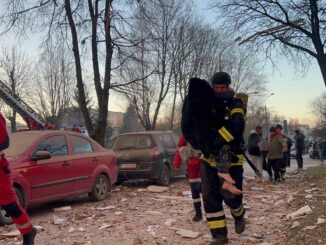Bombeiro ucraniano carrega uma criança ferida entre escombros após ataque russo contra área residencial.