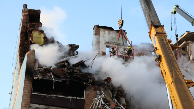 Equipes de resgate trabalham entre escombros e fumaça em prédio destruído após ataque em Ternopil, com guindastes auxiliando na busca por sobreviventes.