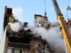 Equipes de resgate trabalham entre escombros e fumaça em prédio destruído após ataque em Ternopil, com guindastes auxiliando na busca por sobreviventes.