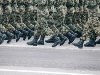 Soldados em uniforme camuflado marchando em formação sobre uma rua asfaltada.