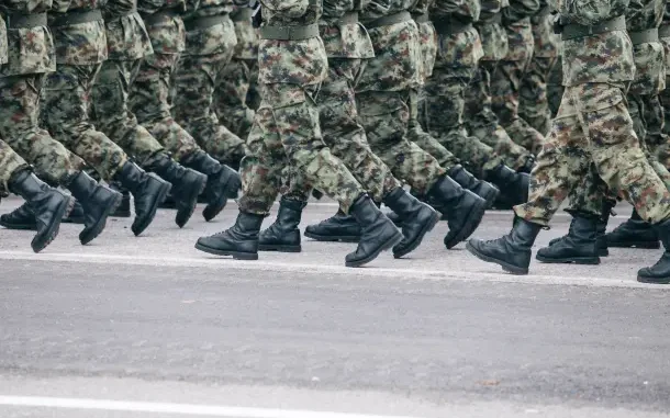 Soldados em uniforme camuflado marchando em formação sobre uma rua asfaltada.