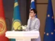 Representante da União Europeia discursa em fórum sobre o Corredor de Transporte Transcaspiano em Tashkent, com bandeiras da UE e de países da Ásia Central ao fundo.